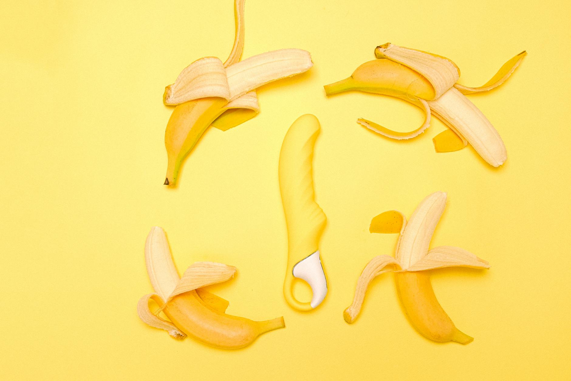 Yellow silicone vibrator surrounded by fresh lemons on a bright yellow background.