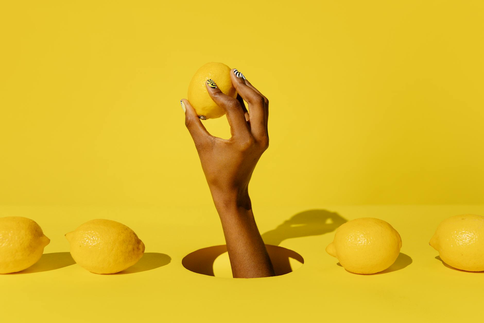 A hand holding a lemon against a vivid yellow background, symbolizing fresh pleasure and vitality