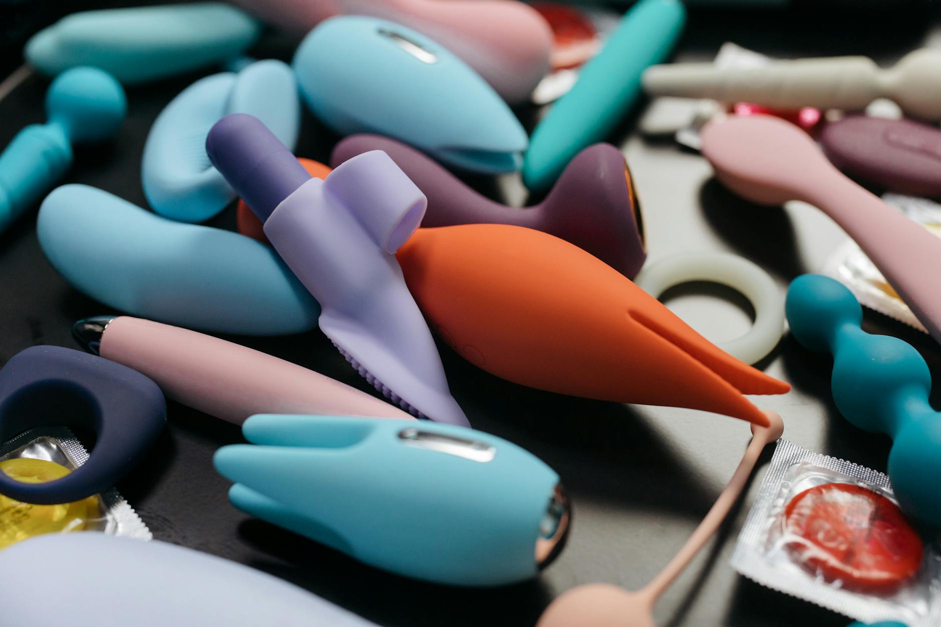 Two hands holding pink and blue silicone clitoral vibrators against a pastel background