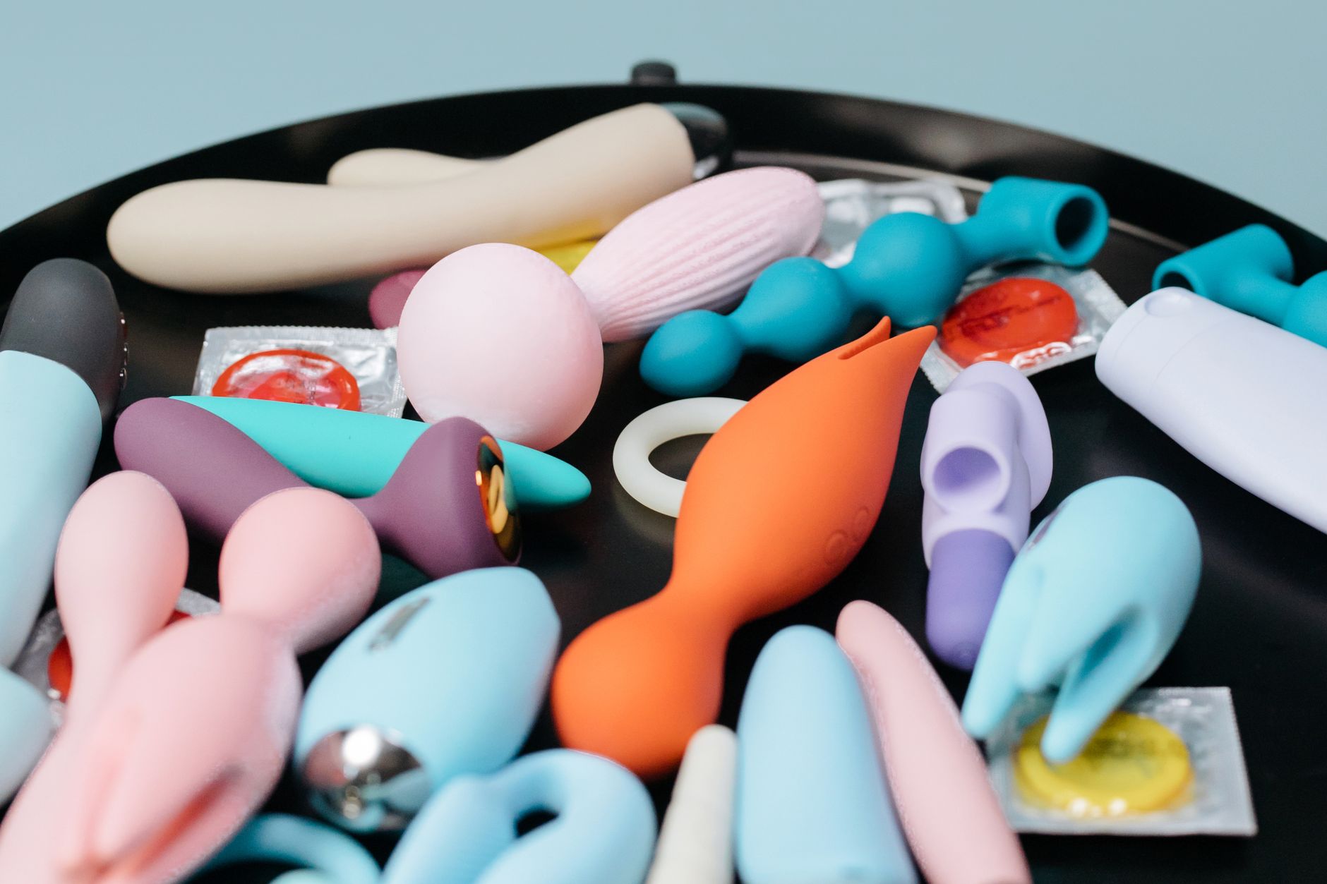 Woman with eyeglasses holding blue and pink silicone vibrators in a contemplative manner.