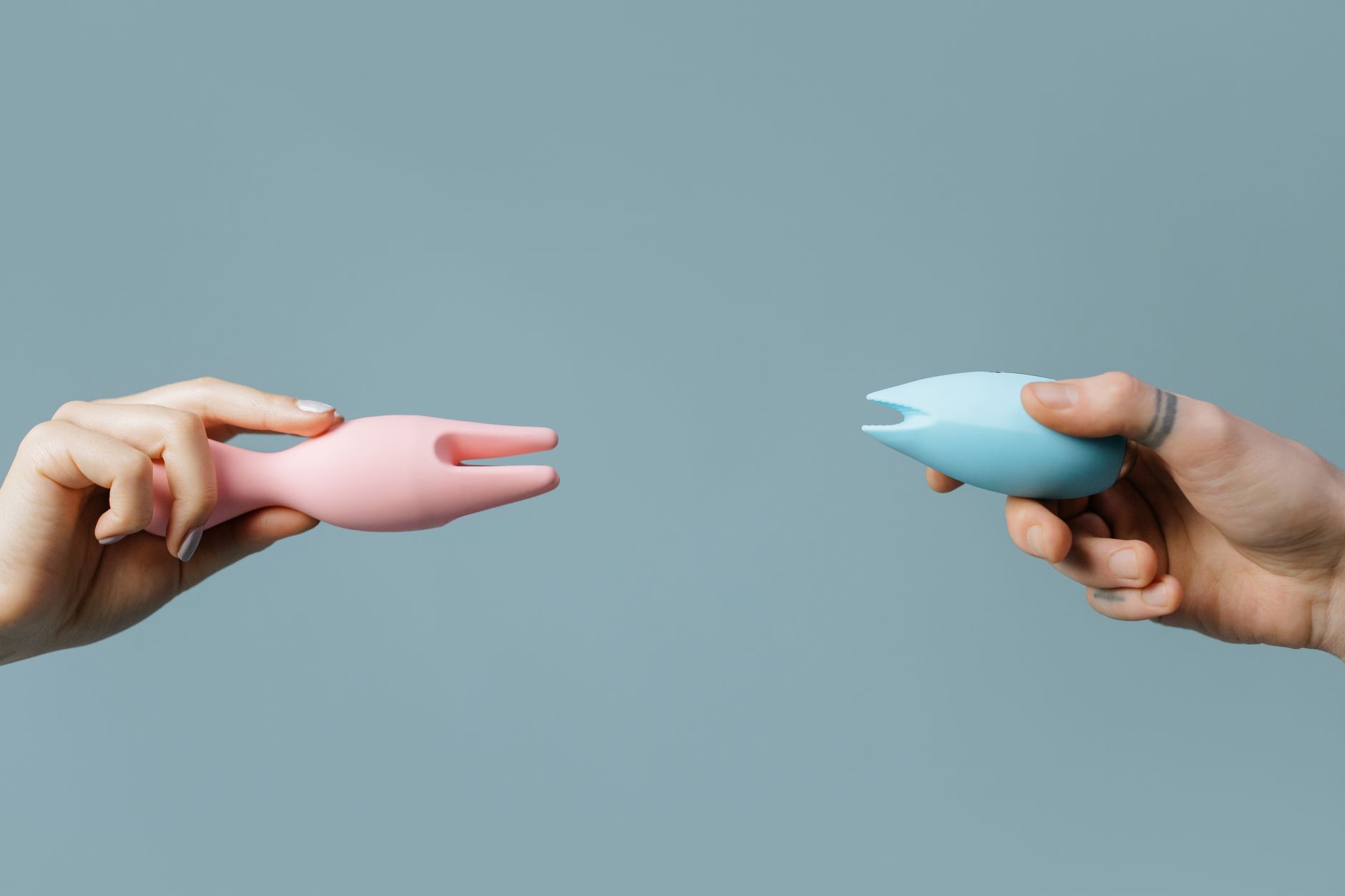 Woman holding pink and blue silicone vibrators against a pastel background.