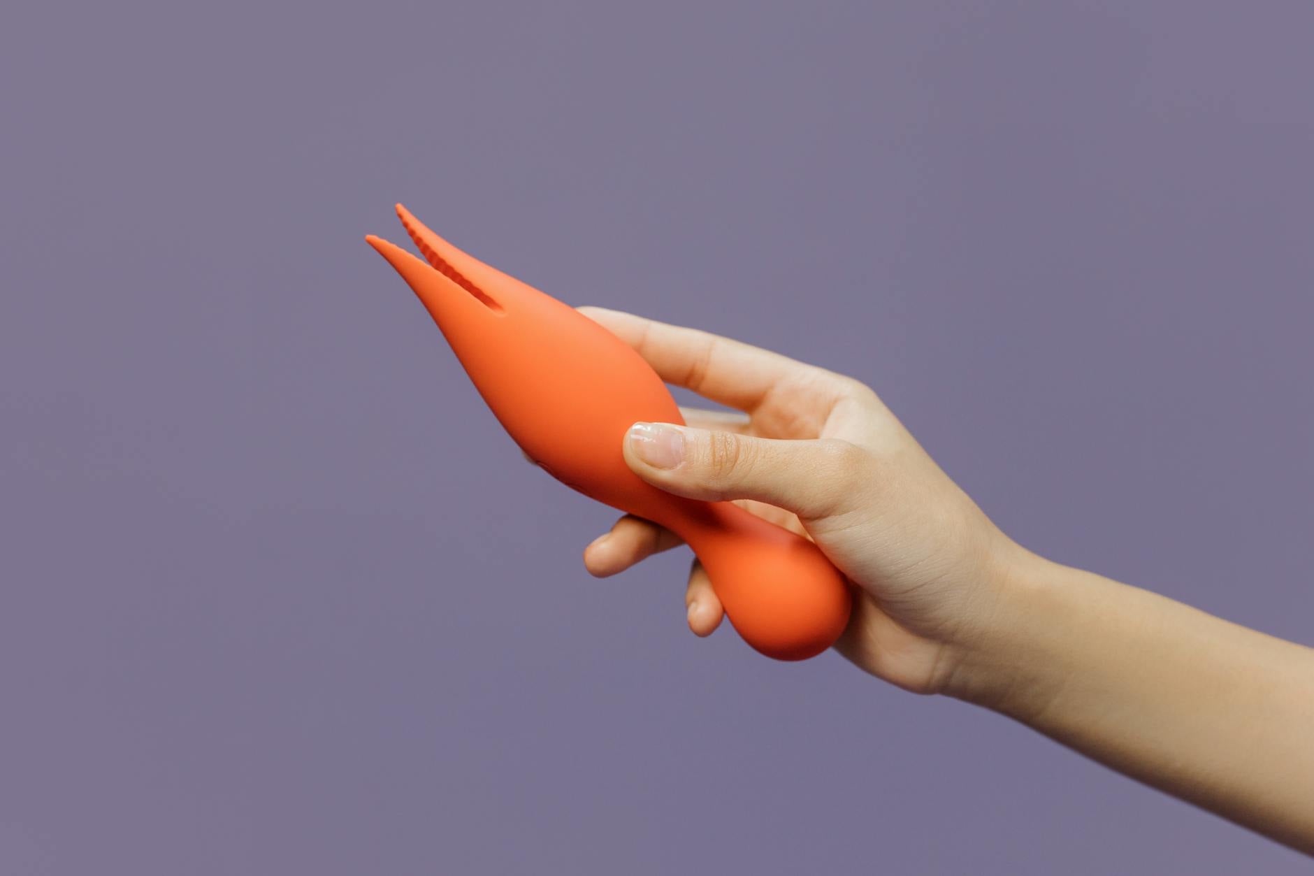 A hand holding a vibrant clitoral vibrator, showcasing sensuality and self-care