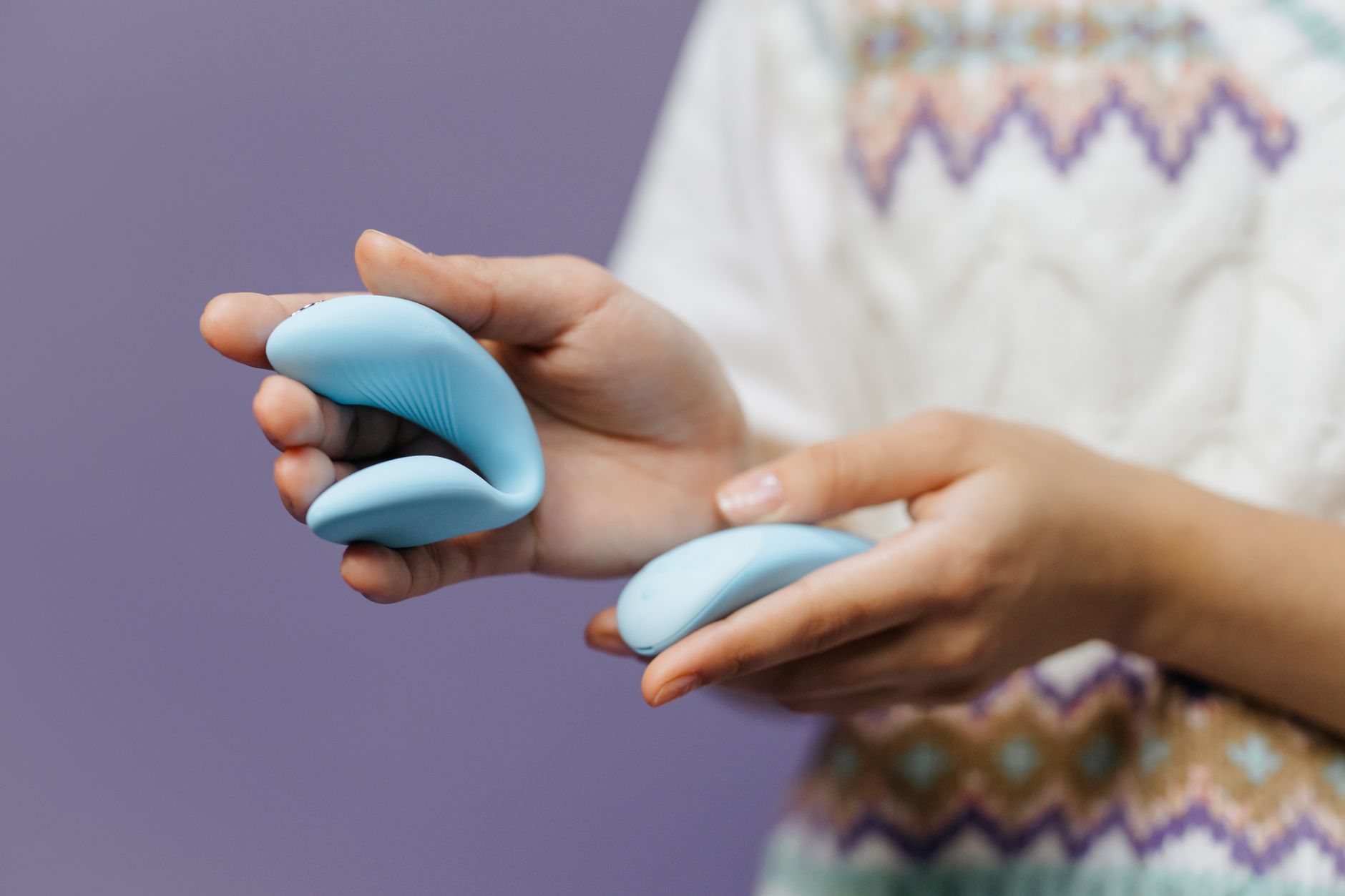 Intimate close-up of hands holding a sleek blue vibrator against a purple background, showcasing modern sensuality.