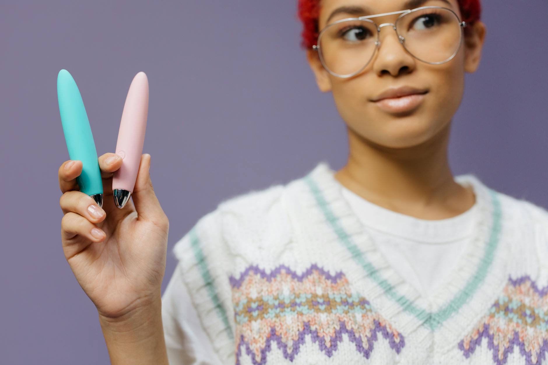 A woman holding two colorful vibrators against a purple background, representing options for early menopause pleasure