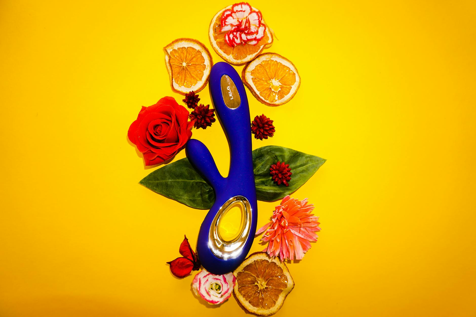 A blue lemon vibrator surrounded by flowers and citrus on a yellow background, symbolizing rediscovery and fresh pleasure.